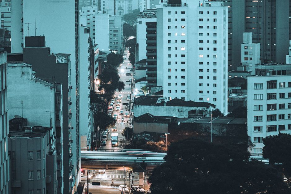 Vista urbana de uma cidade com prédios altos e ruas movimentadas ao entardecer, transmitindo o tema de urbanismo e vida na cidade.