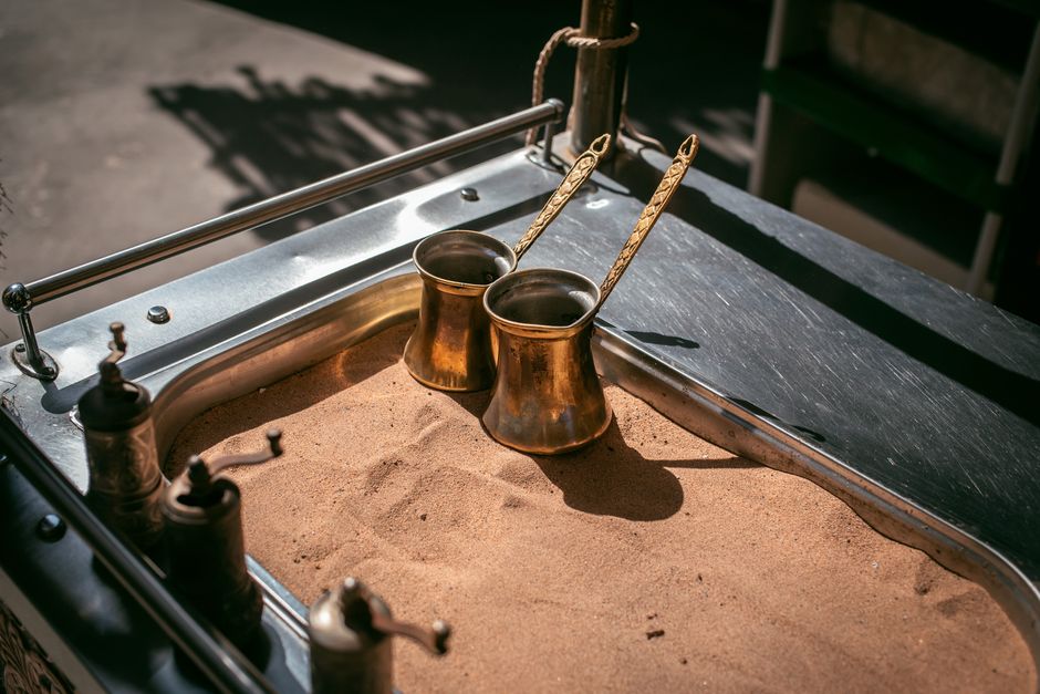 Cafeteira tradicional na areia, indicando uma experiência de preparo do café ao ar livre.