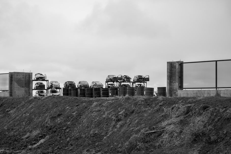 Imagem de uma instalação de armazenamento de veículos, com vários carros parados em plataformas elevadas, sob céu nublado, sugerindo temas de logística ou armazenamento de automóveis.