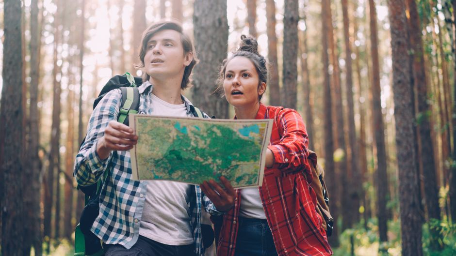 Jovens explorando a natureza ao verificarem um mapa durante uma trilha na floresta, demonstrando aventura e descoberta.
