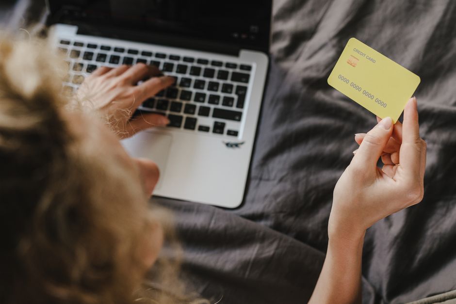 Pessoa realizando compras online, utilizando um laptop e cartão de crédito, em um ambiente doméstico.