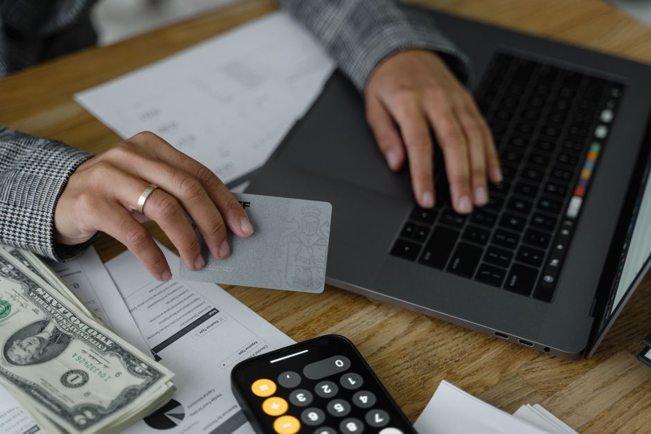 Imagem de uma pessoa realizando uma transação financeira com cartão de crédito, gadgets e documentos de negócio, ilustrando gestão financeira e planejamento empresarial.