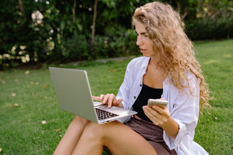 Mulher ao ar livre usando laptop e smartphone, simbolizando trabalho remoto e conectividade.