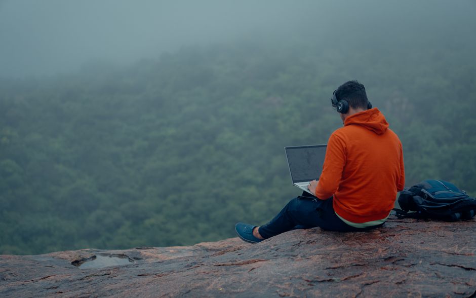 Homem trabalhando em um laptop ao ar livre em um ambiente natural, simbolizando conexão com a natureza e produtividade remota.