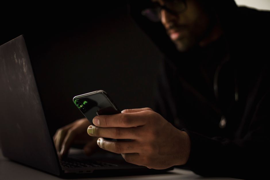 Pessoa concentrada usando smartphone em ambiente escuro, possivelmente para comunicação ou pesquisa online.