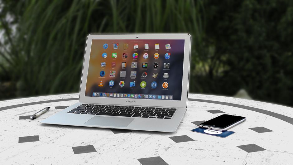 Imagem de um laptop e smartphone sobre uma mesa ao ar livre, simbolizando trabalho remoto ou tecnologia móvel.