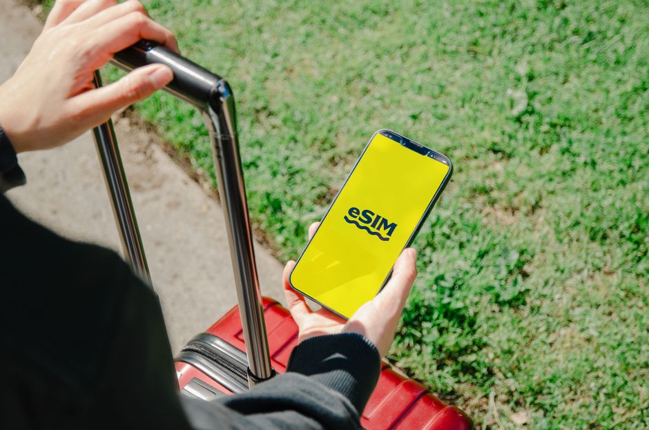 Pessoa segurando um telefone com o logo da WISE em um ambiente externo com grama, sugerindo viagens ou uso de tecnologia para negócios.
