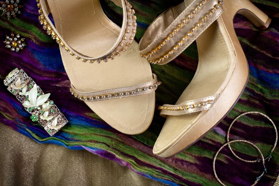 Sapatos de festa decorados com pedras e acessórios de uso em ocasiões especiais, dispostos sobre um tecido colorido.