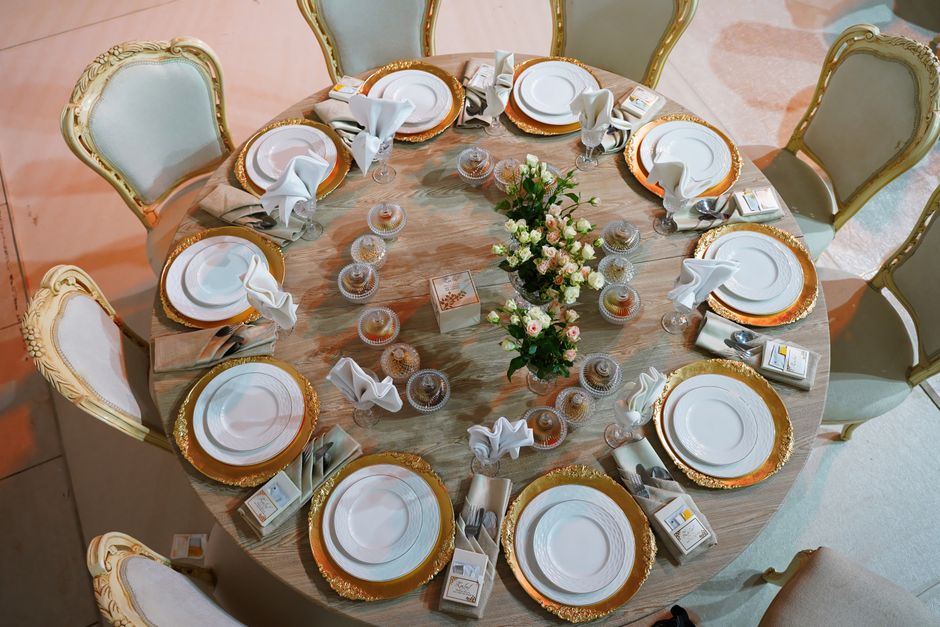 Mesa de jantar decorada para uma celebração elegante, com pratos, talheres, taças e centro de flores estilizado.