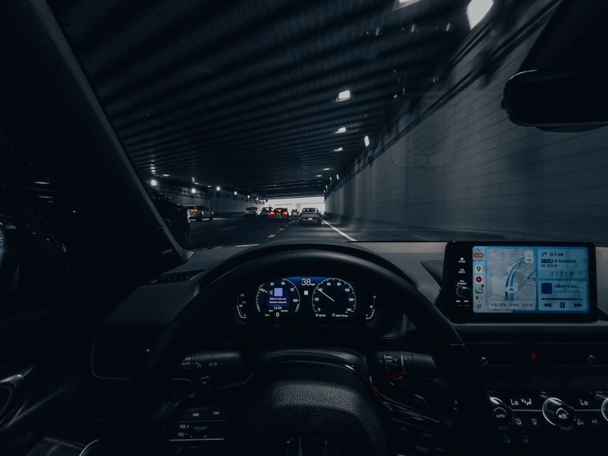Imagem de dentro de um carro dirigindo por um túnel à noite, com foco na tela de navegação e painel de instrumentos.