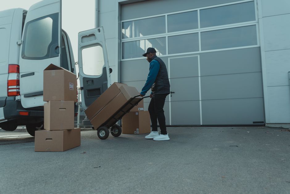 Pessoa carregando caixas de uma van em um ambiente de entrega ou logística ao ar livre.