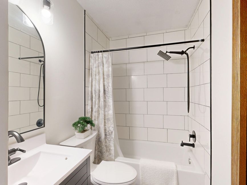 Banheiro moderno com revestimento em azulejos brancos, espelho grande e detalhes de decoração minimalista.