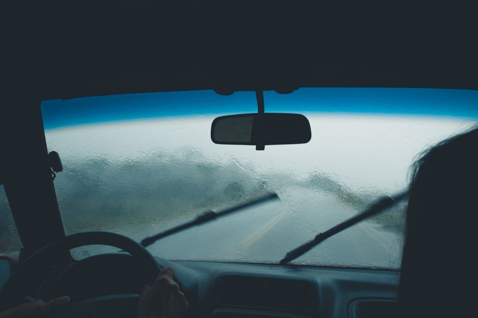 Imagem de uma vista de dentro de um veículo durante uma forte chuva, com o motorista ao volante enfrentando a tempestade na estrada.