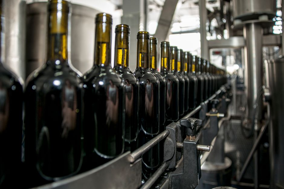 Imagem de garrafas de vinho sendo produzidas em uma linha de montagem industrial, destacando o processo de fabricação na vinícola.