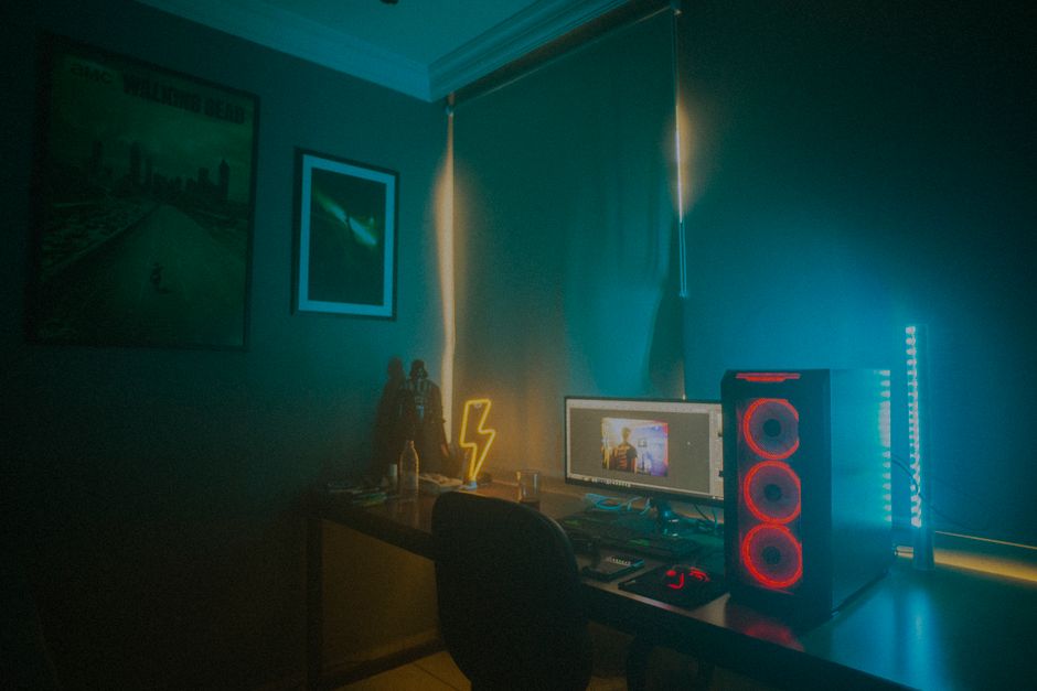 Espaço de trabalho com iluminação neon e equipamentos de computador, sugerindo um ambiente de produção ou gaming com atmosfera tecnológica e moderna.