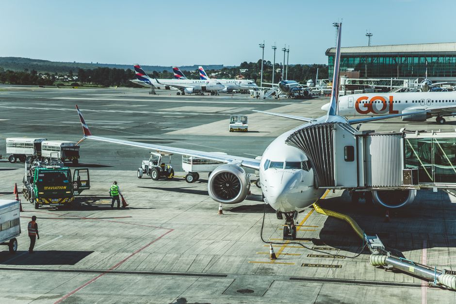Imagem de um aeroporto com aviões estacionados e equipes de infraestrutura preparando uma aeronave para decolagem, ideal para artigos sobre transporte aéreo ou gestão de aeroportos.