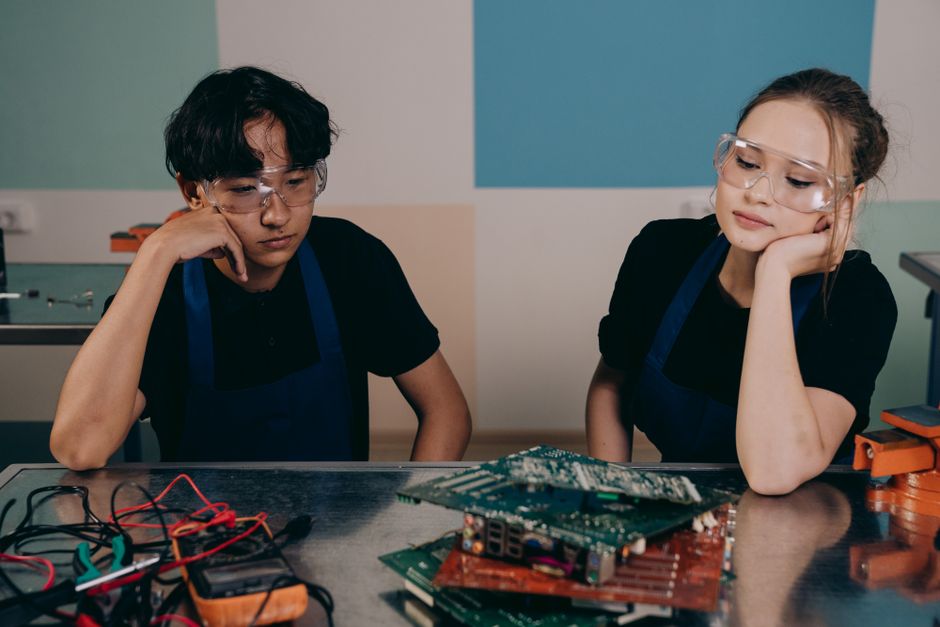 Duas crianças em um ambiente de aprendizado, manipulando componentes eletrônicos e experimentos científicos, demonstrando interesse na tecnologia e inovação.