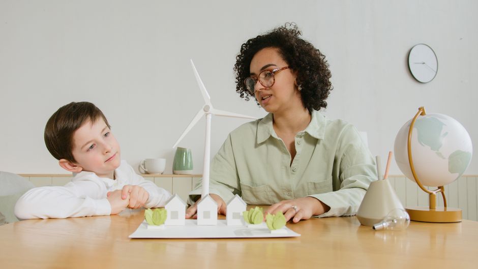 Mulher e criança discutindo energias renováveis e sustentabilidade em um ambiente de estudo ou trabalho, com modelos de turbinas e elementos relacionados ao tema.