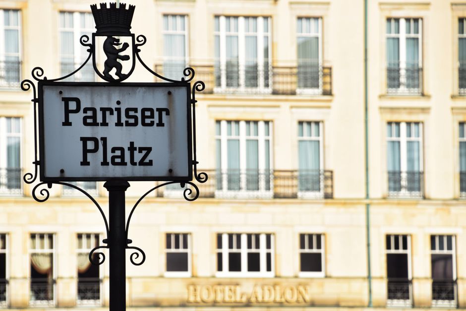 Sinal de rua com o nome 'Pariser Platz' em frente a edifícios históricos em Berlim, representando turismo urbano e arquitetura da cidade.