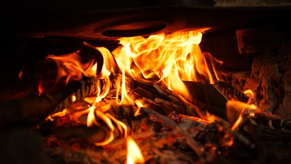 Imagem de uma fogueira com fogo intenso e pedaços de madeira queimando, destacando o calor e a combustão.
