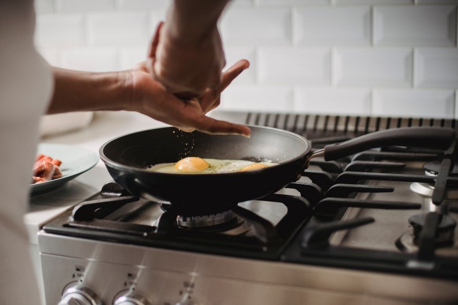 Pessoa preparando ovos na frigideira em uma cozinha moderna, simbolizando alimentação e rotina culinária.