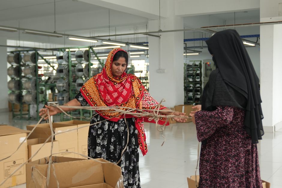 Duas mulheres observando produtos e embalagens em um ambiente de fábrica ou armazém, destacando o trabalho artesanal ou de produção em escala industrial.