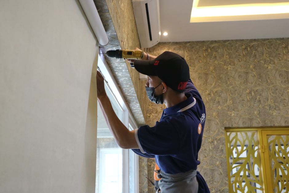 Homem instalando ou ajustando uma persiana ou cortina em uma janela de ambiente interno, com foco na manutenção residencial ou decoração de interiores.