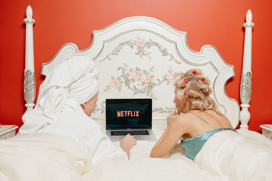 Duas mulheres na cama assistindo a Netflix, com uma diferente e divertida rotina de manhã.