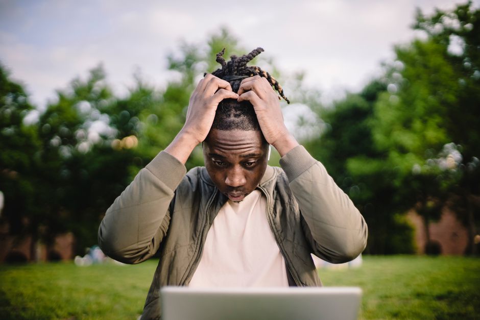 Homem preocupado olhando para o computador ao ar livre, ilustrando estresse ou ansiedade relacionada a tecnologia ou trabalho.