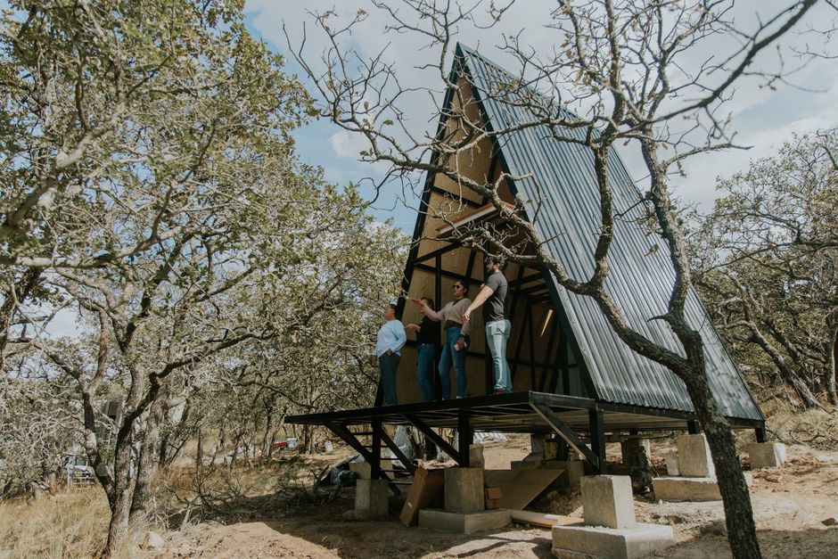 Grupo de pessoas avaliando a construção de uma casa sustentável em uma área com árvores e natureza ao redor.