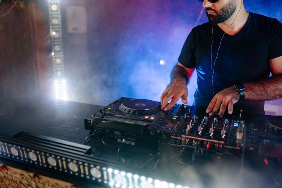 DJ deitado em um palco com equipamentos de som, criando uma atmosfera de festa e música ao vivo.