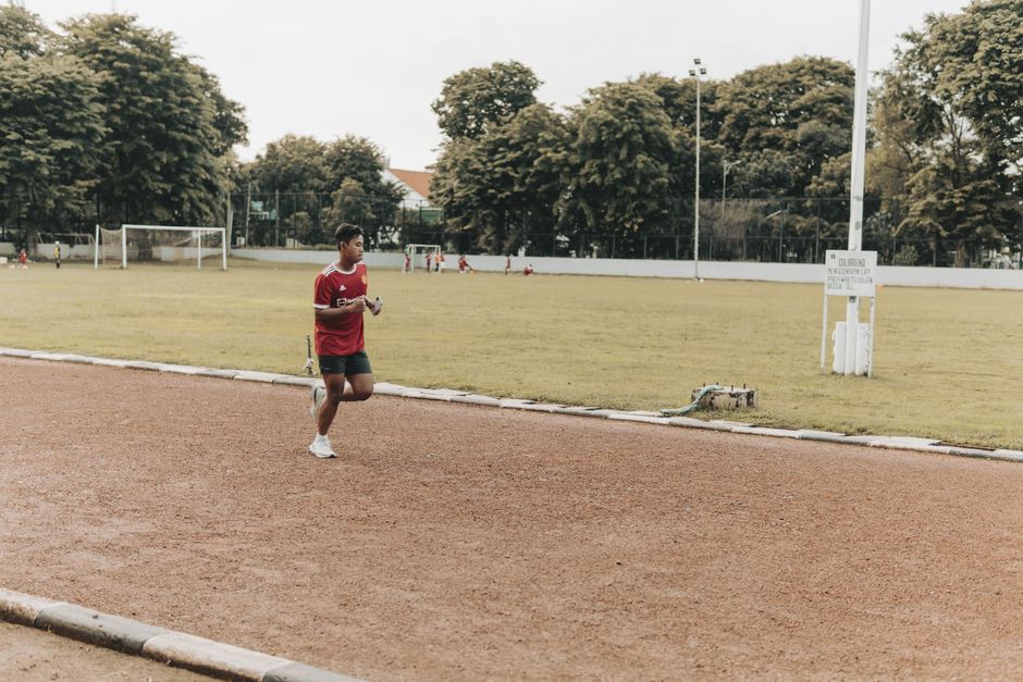Jovem correndo em uma pista de atletismo ao ar livre, representando esforço e saúde em contexto esportivo.