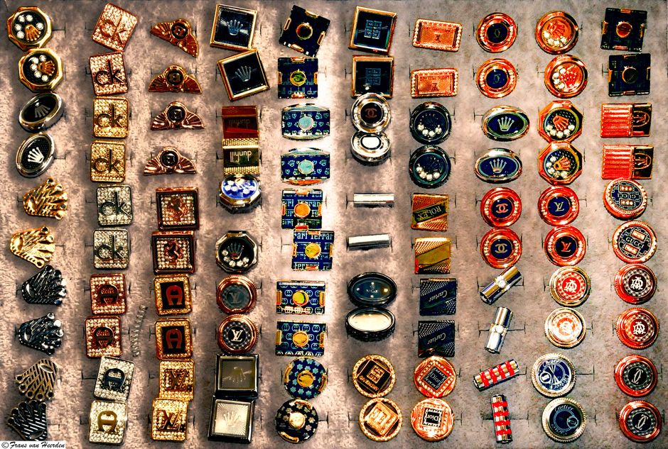 Coleção de botões decorativos com diversas cores, formas e detalhes, dispostos em linhas sobre uma superfície de mesa de vidro.