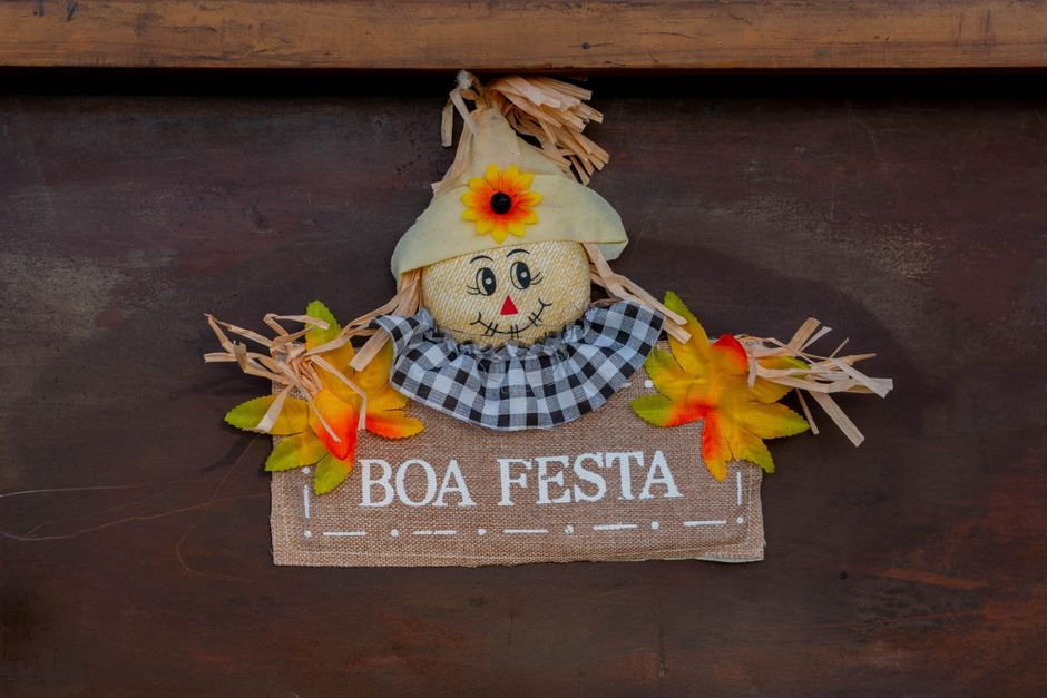 Imagem de uma decoração de festa com um boneco de palhaico, folhas coloridas e um banner que deseja "Boa Festa", ideal para artigos sobre celebrações tradicionais.