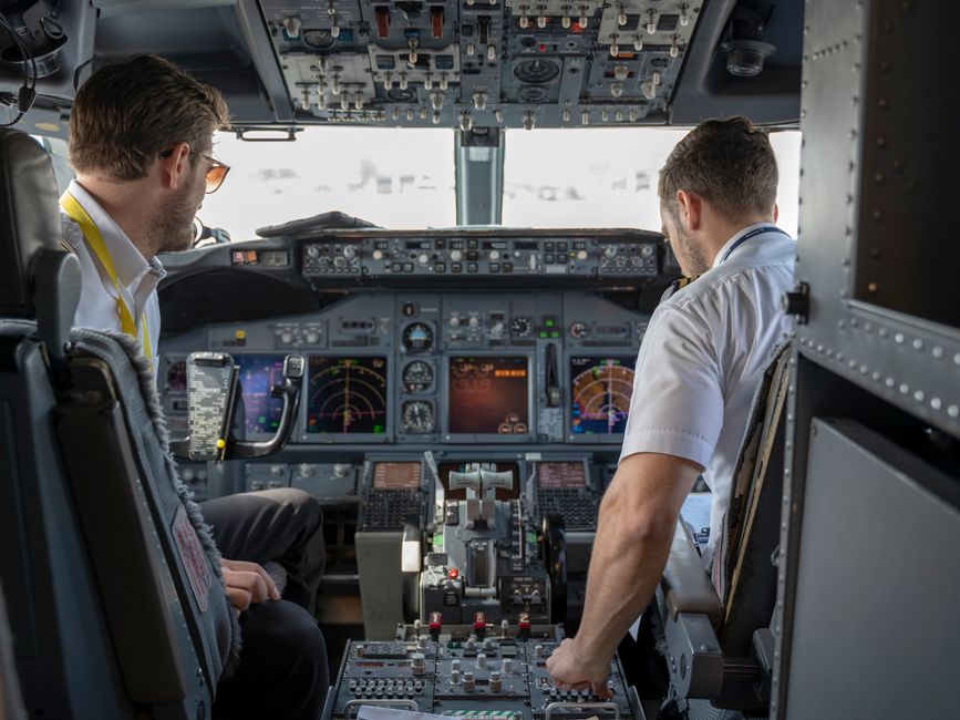 Imagem de dois pilotos dentro da cabine de um avião, focados nos instrumentos e controles da aeronave, representando o setor de aviação e sistemas de comando.