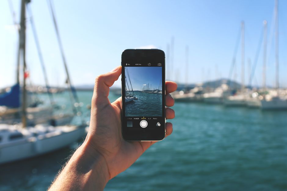 Pessoa usando um smartphone para tirar uma foto de um marina com veleiros, transmitindo o tema de fotografia e lazer no mar.