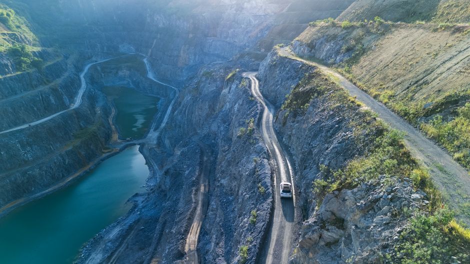 Imagem de uma estrada sinuosa ao lado de um grande reservatório de água, em meio a um cenário montanhoso, simbolizando aventura e exploração na natureza.
