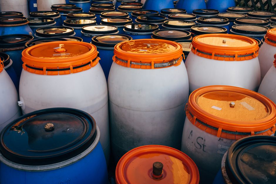 Imagem de vários tambores plásticos coloridos empilhados, utilizados para armazenamento de líquidos ou produtos industriais.