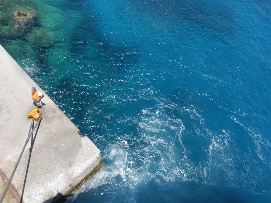 Marinheiro realizando manutenção em estrutura de cais com vista para o mar azul, representando segurança e trabalho marítimo.