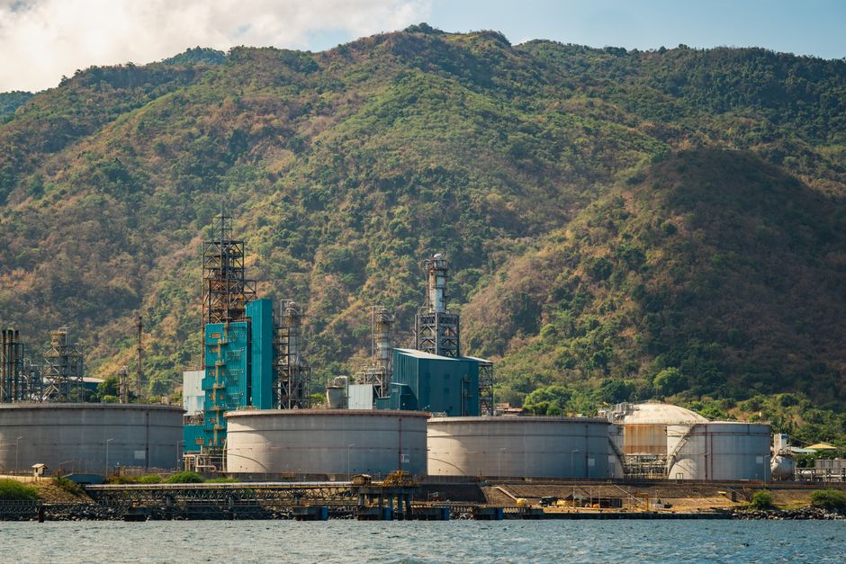 Imagem de uma usina industrial com uma cadeia de montanhas ao fundo, destacando o impacto da indústria na natureza.