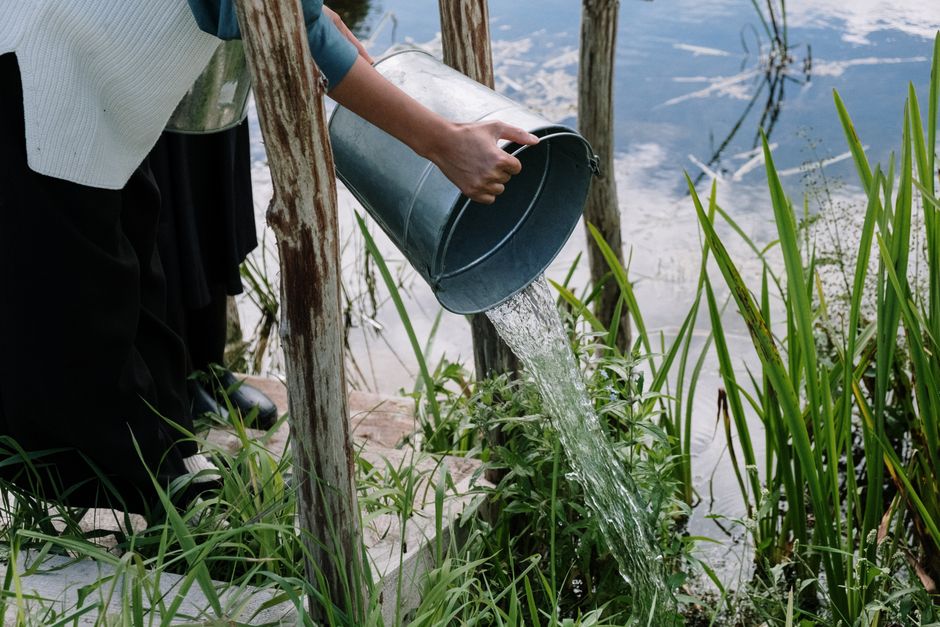 Pessoa coletando água de um lago ou represa em um ambiente natural, simbolizando sustentabilidade ou uso de recursos naturais.