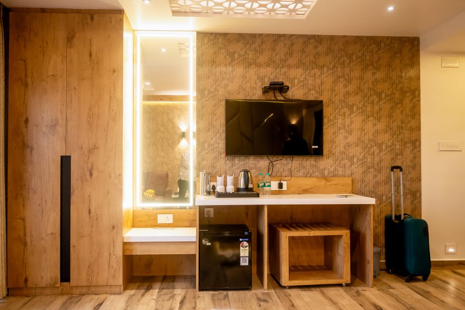 Imagem de um espaço de hotel com área de entretenimento e minibar, destacando uma parede de acabamento amadeirado e uma televisão.