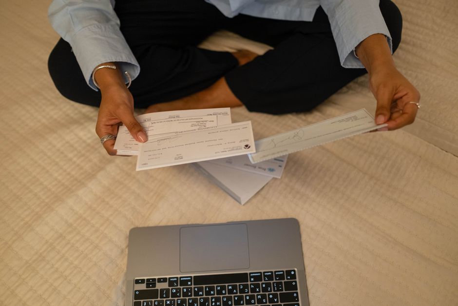 Pessoa organizando cheques e documentos financeiros enquanto trabalha no computador, ilustrando planejamento financeiro e gestão de recursos.