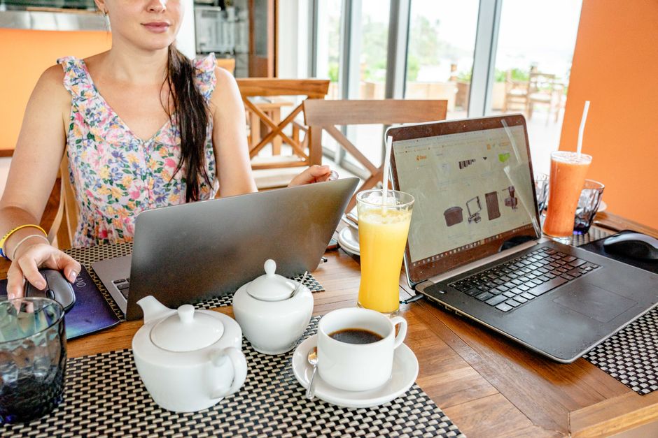 Mulher trabalhando em um ambiente de coworking, com laptops e bebidas, focando em produtividade e ambiente de trabalho colaborativo.