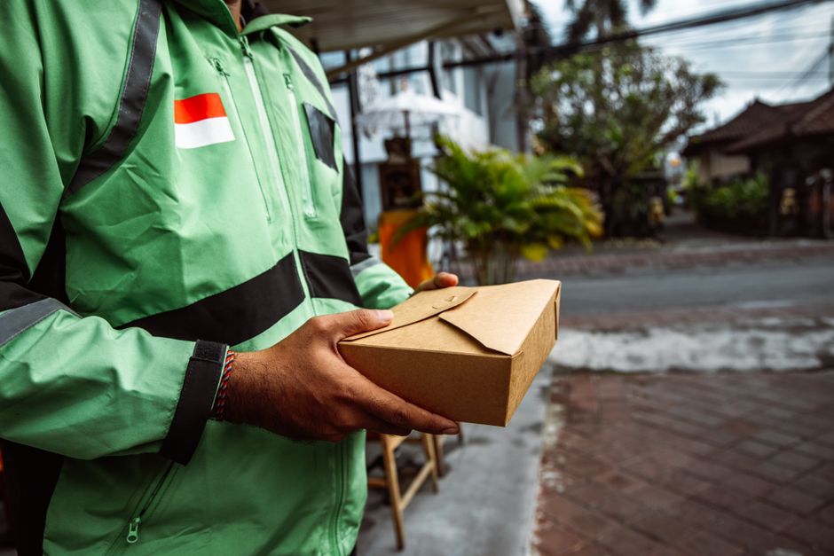 Pessoa entregando uma encomenda de comida para entrega por delivery na rua.