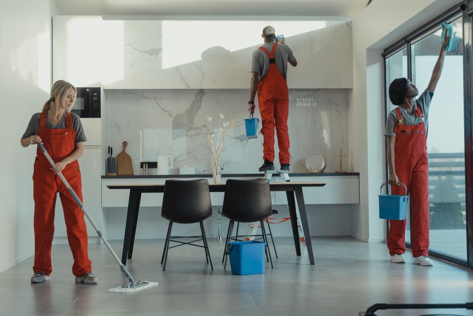 Equipe de limpeza realizando manutenção em uma cozinha moderna com iluminação natural e design clean.