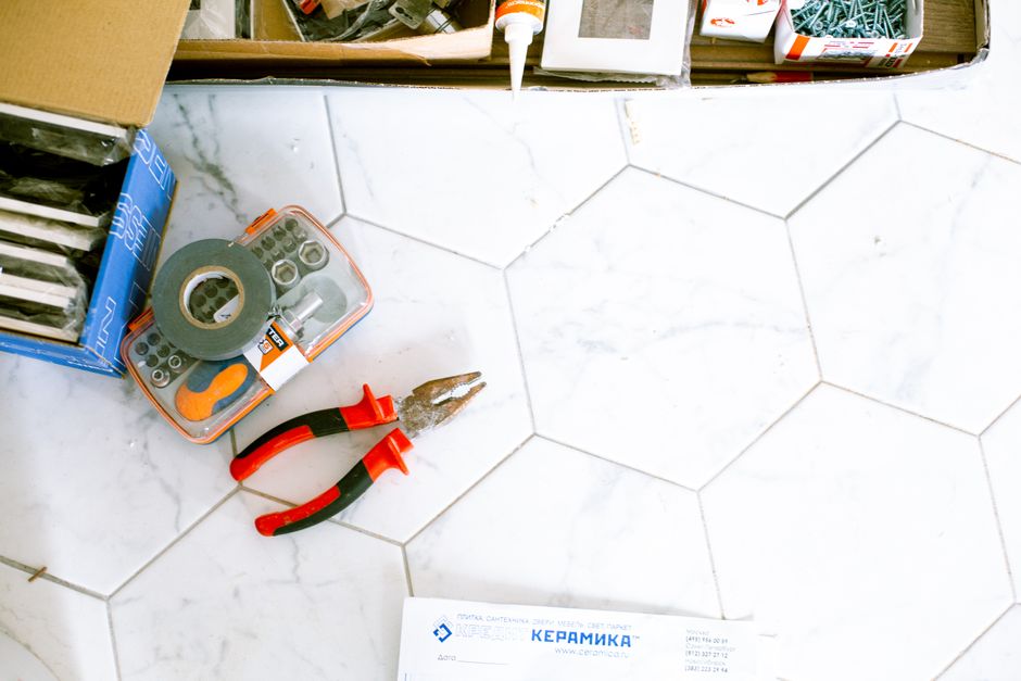 Imagem de um piso de azulejos brancos com ferramentas de manutenção ao lado, sugerindo reforma ou reparo em residência ou estabelecimento comercial.