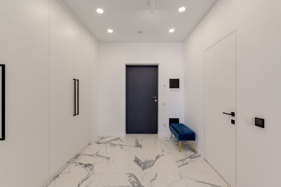 Corredor de entrada moderno e minimalista com acabamento em mármore claro e detalhes em preto e azul marinho.