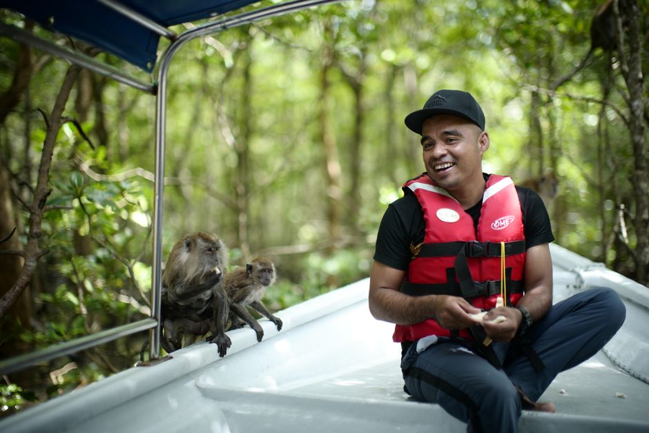 Homem sorridente em um passeio de barco na floresta amazônica, acompanhando macacos próximos à embarcação.