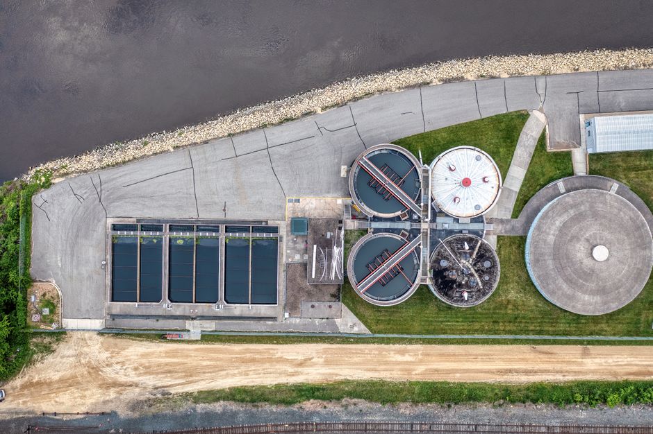 Imagem aérea de uma estação de tratamento de água ou estação de energia, destacando a infraestrutura industrial junto a um rio.